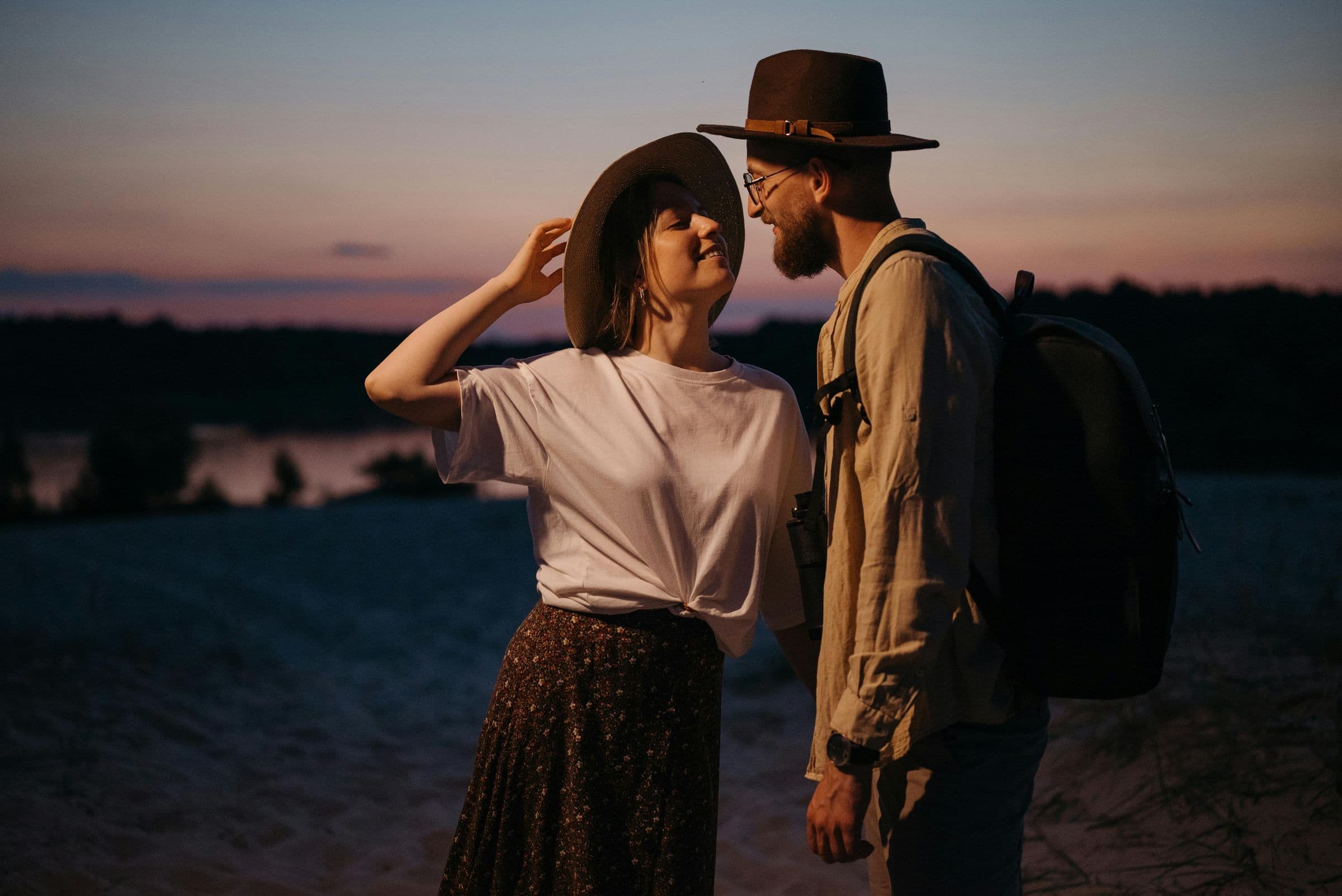 Couple in cowboy hats smiling at each other outdoors at dusk