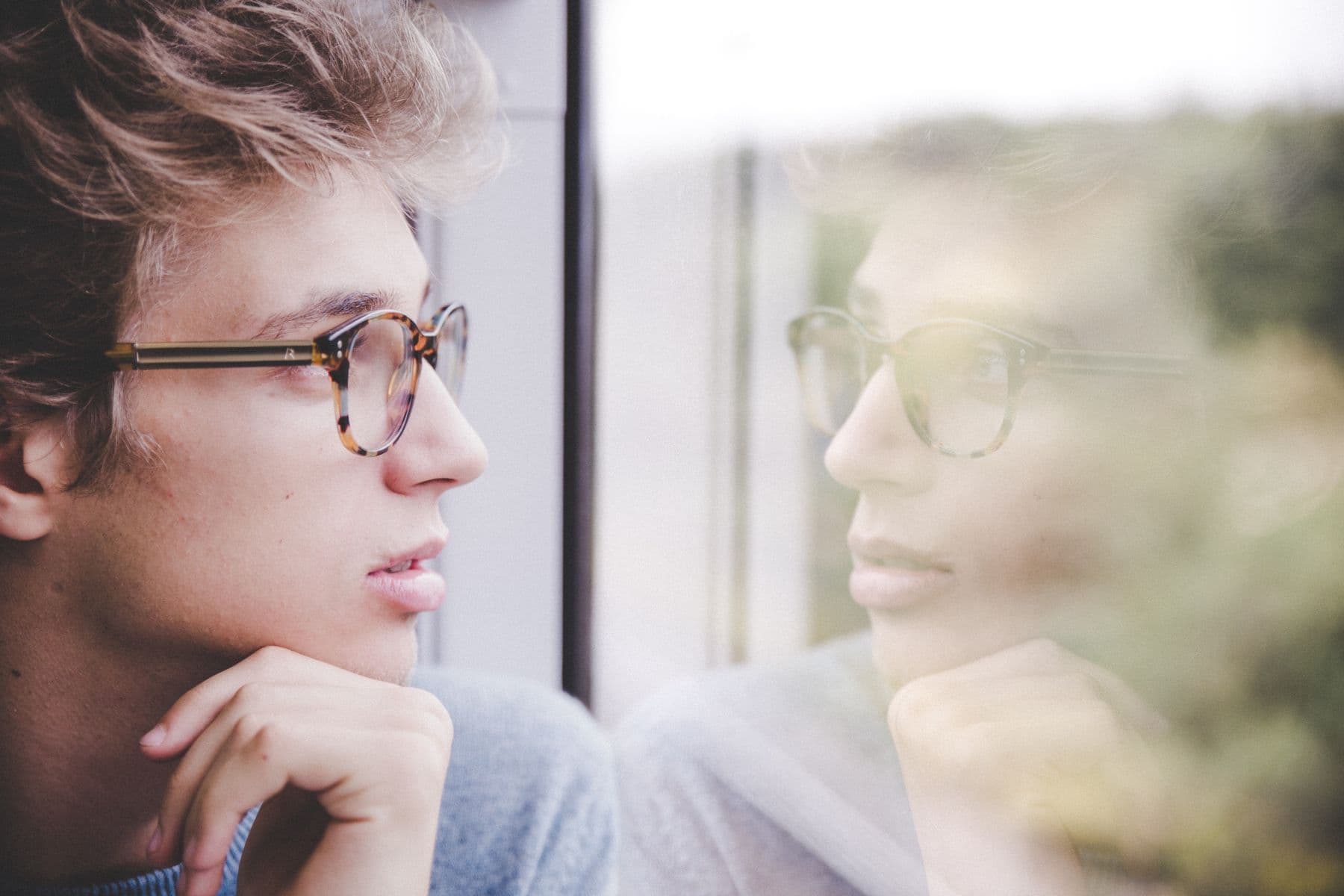 Man's reflection in a window as he looks out, lost in thought