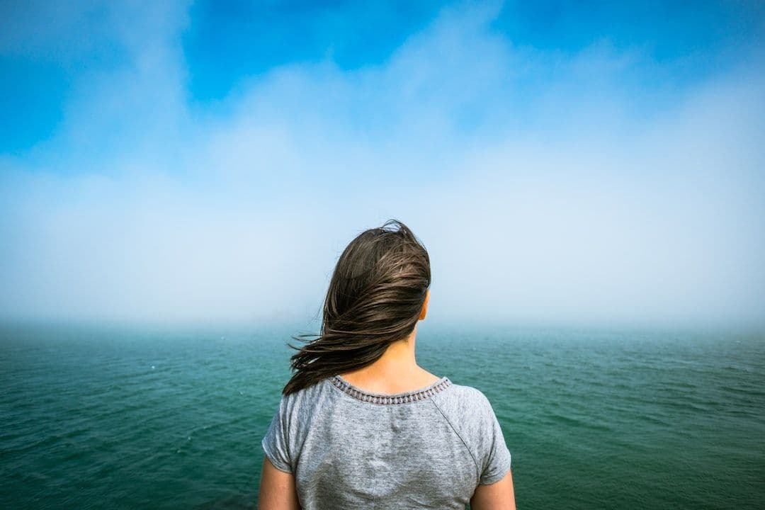 Woman standing at the shore facing the ocean in soft fog