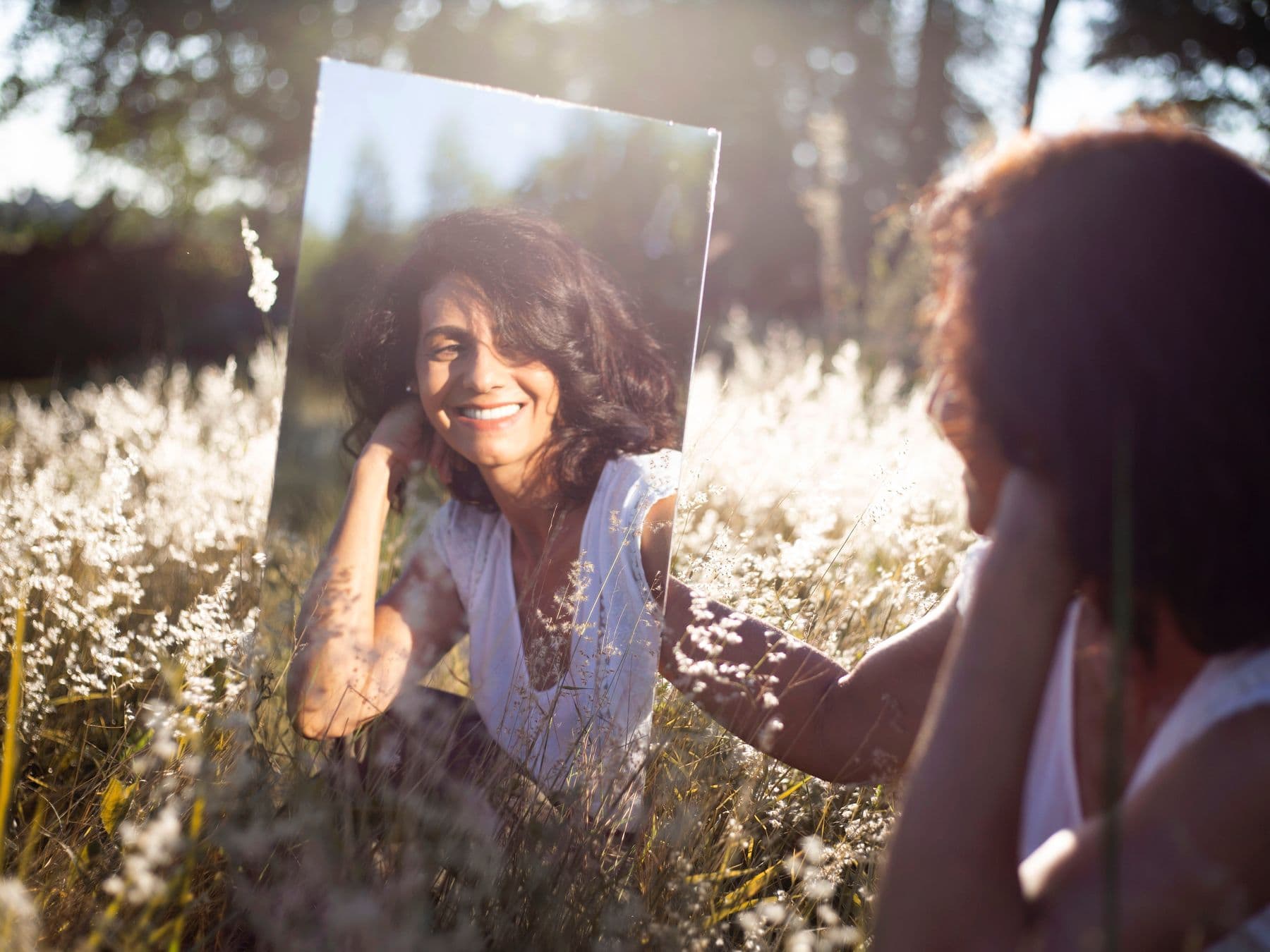 Woman holding a mirror in an open field, reflecting on her identity