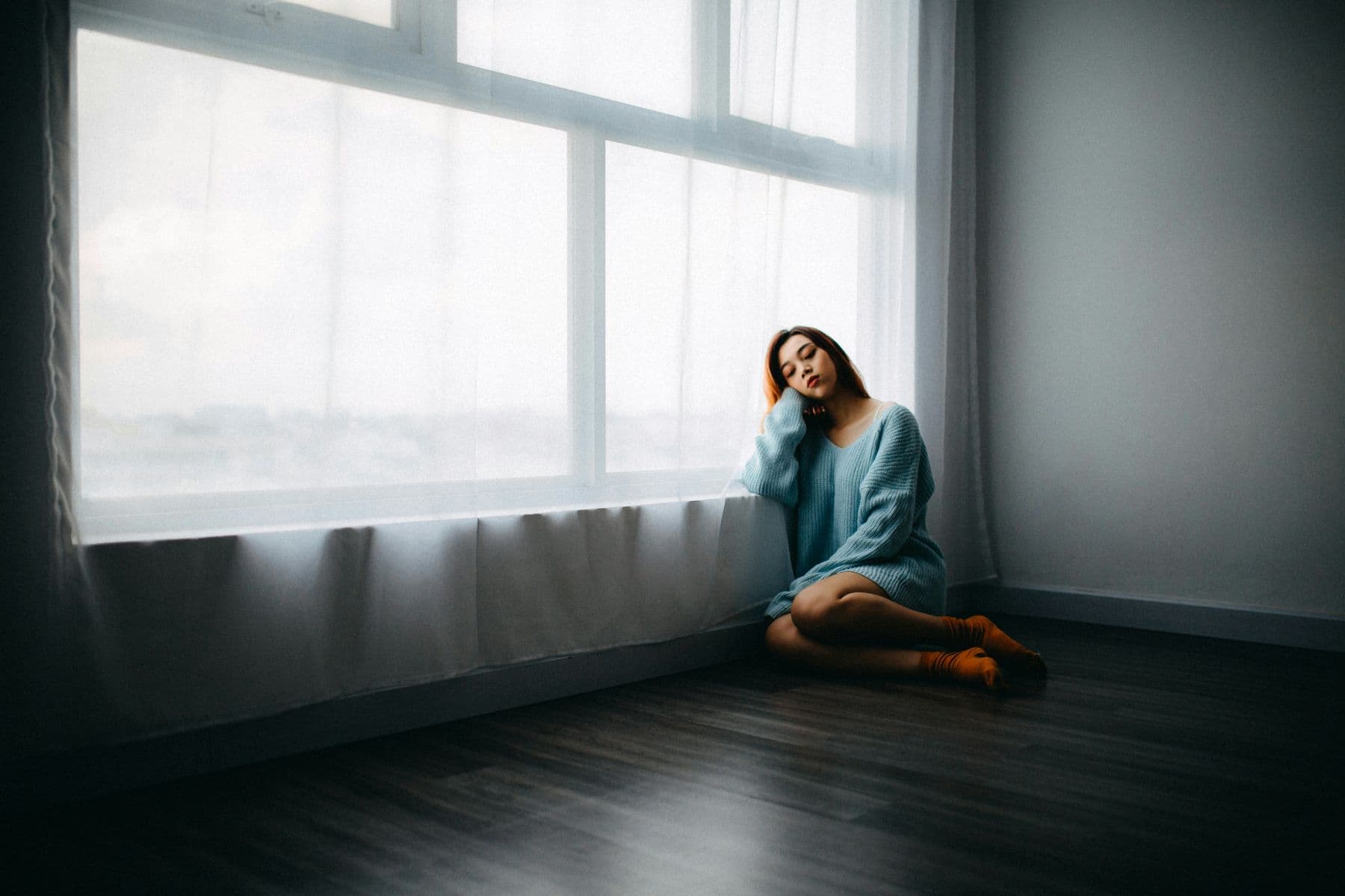 Woman sitting by a sunlit window, reflecting during online individual therapy for Denton adults