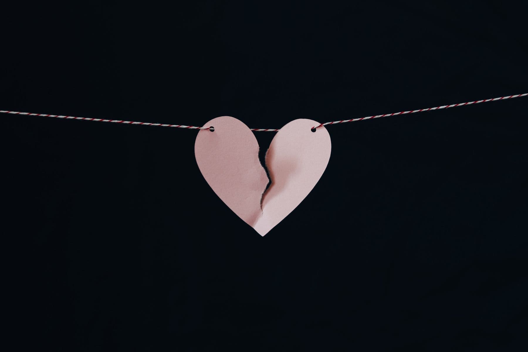 Paper heart torn down the middle, hanging from a string against a dark background