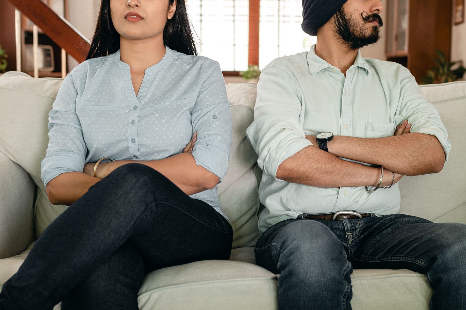 Couple sitting apart on a sofa with their arms crossed after an argument